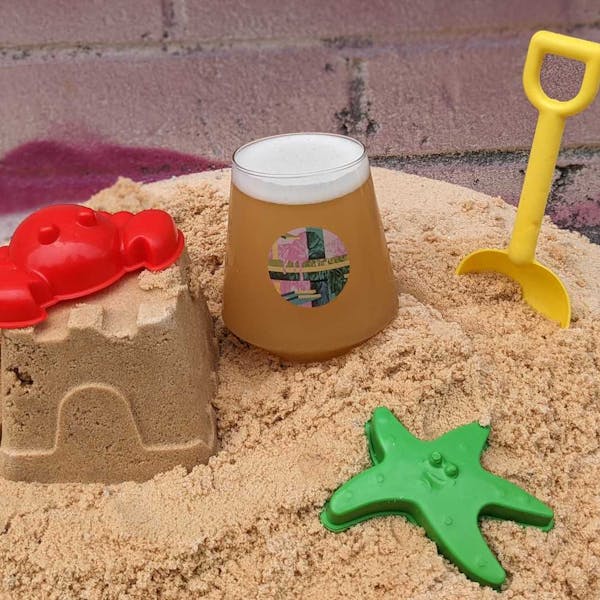 Glass of light beer next to sand castle and beach toys