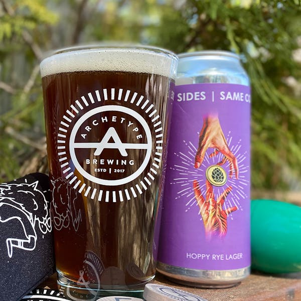 Archetype pint glass with dark beer next to purple can