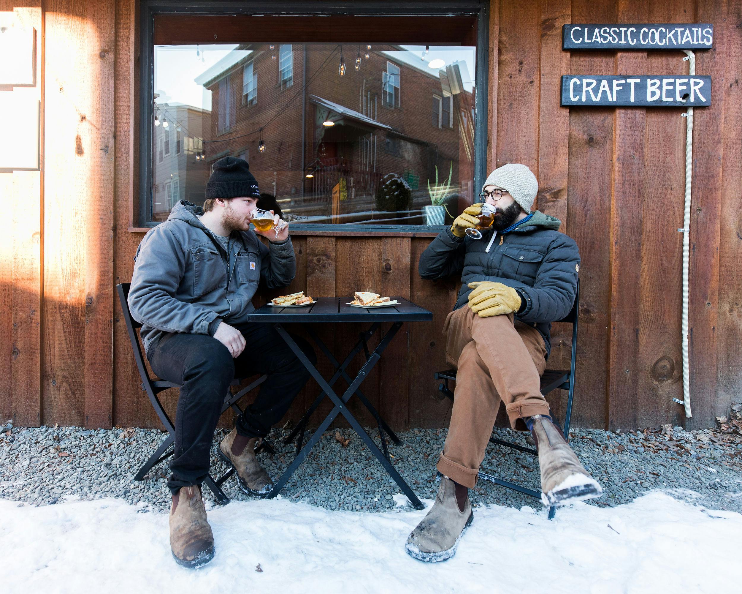 Two customers enjoy a beer outside of the taproom in the snow