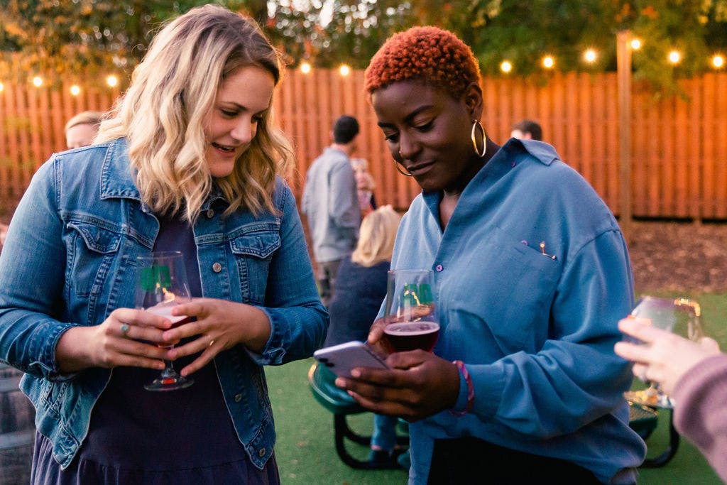 two guests enjoy beers while looking at a phone together