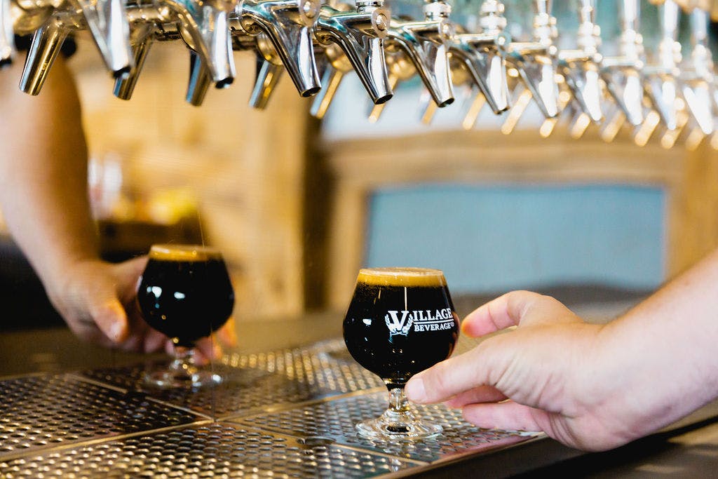 A hand holds a small tasting glass of beer under the taps