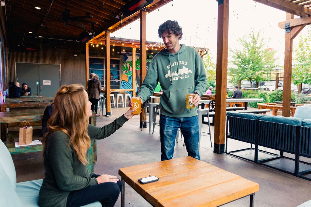 a man hands a woman a beer outside on a patio
