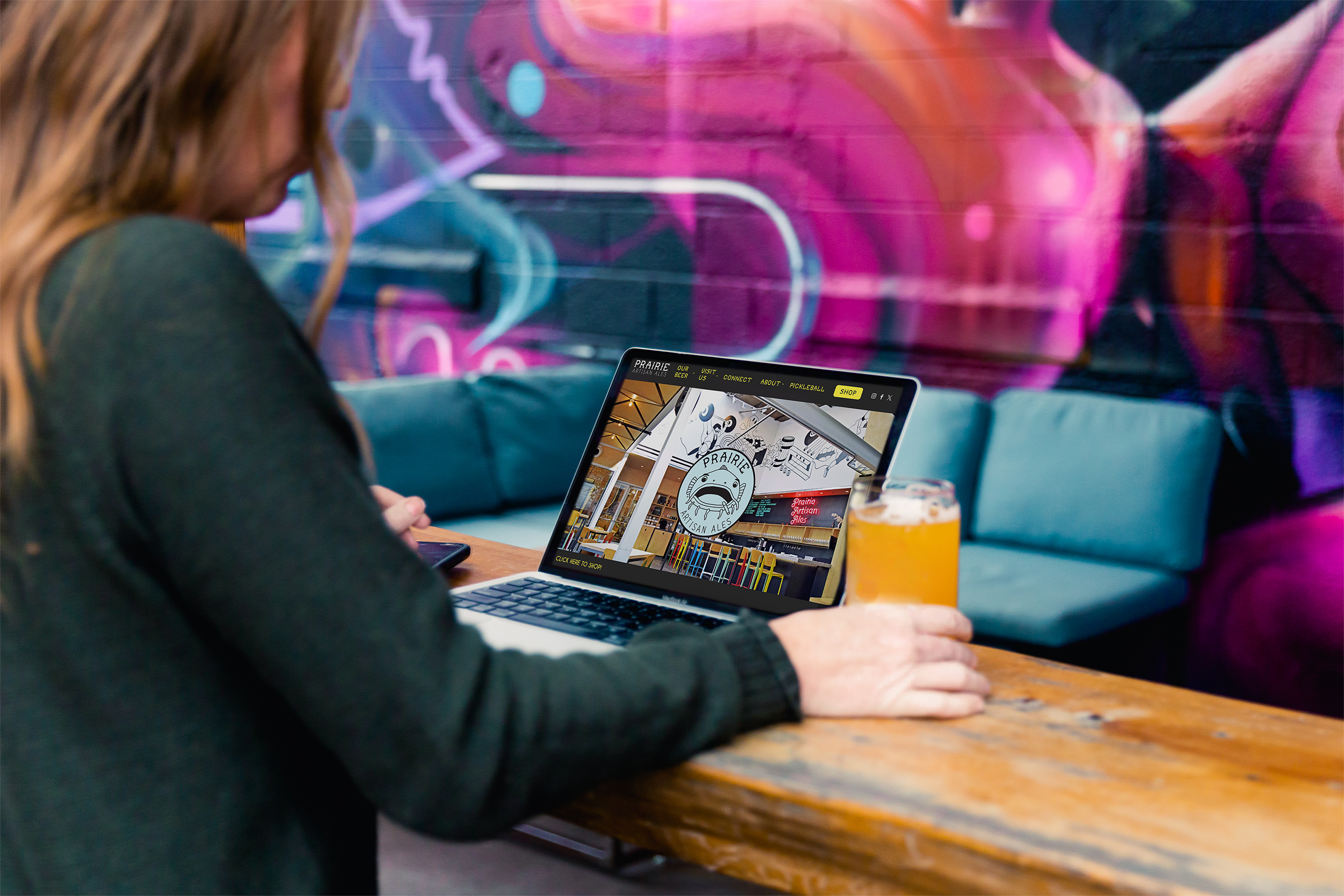 a person sits at a bar with a computer and a beer