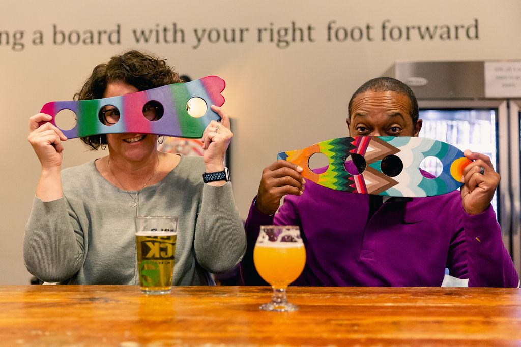 two guests with beers hold up colorful artwork