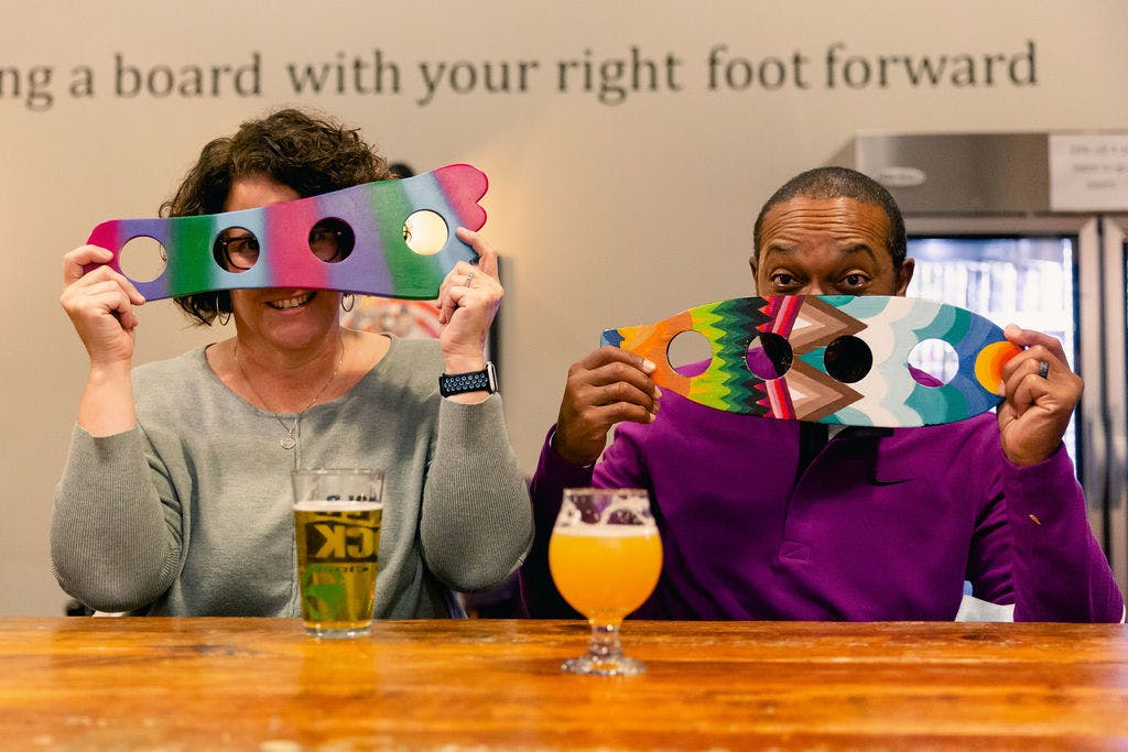 two guests with beers hold up colorful artwork