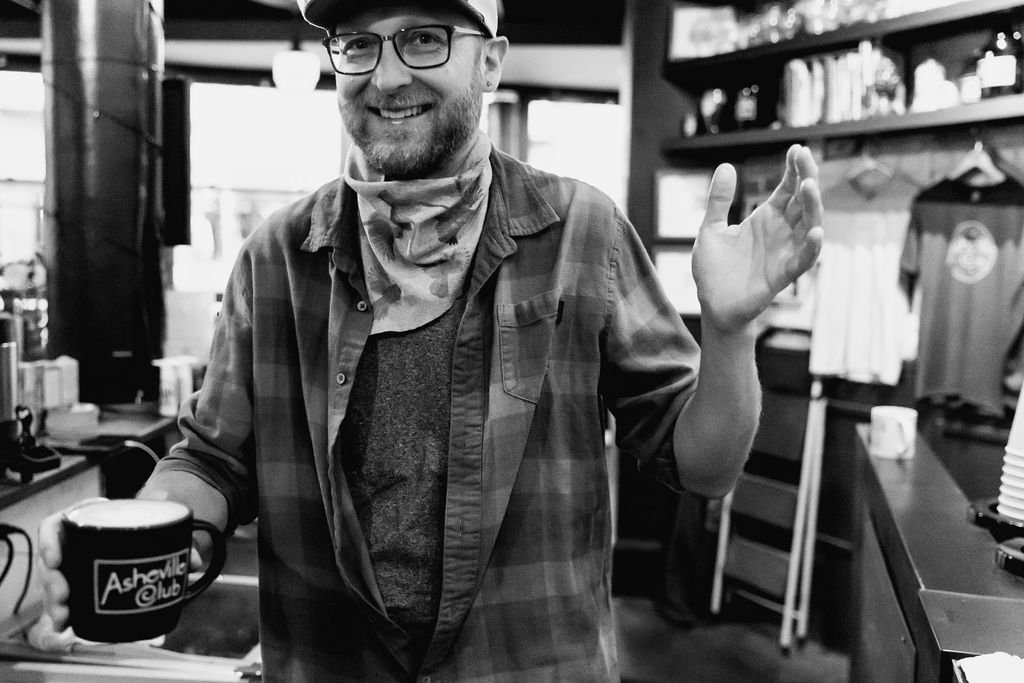 a man in a plaid shirt holds up a glass of beer