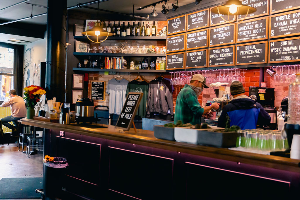 a dimly-lit bar with shelves of glassware and chalkboards 