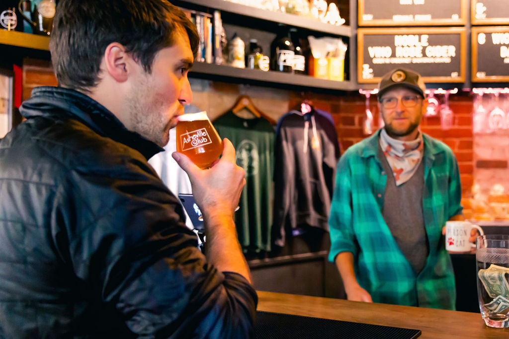 a man sips a beer while shopping for merch at a taproom