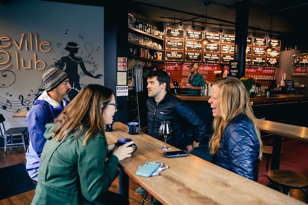 a group of guests smile over beers at a wooden table