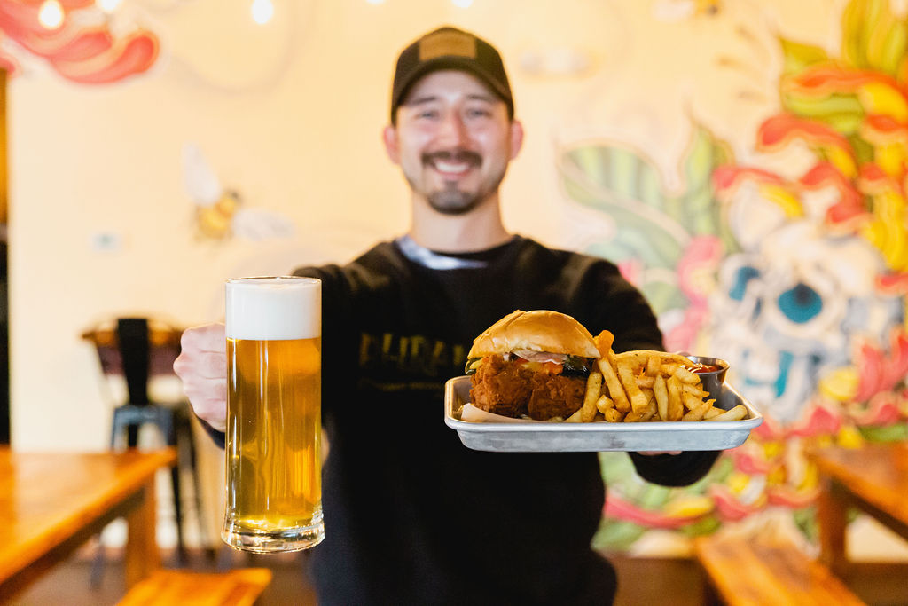 a server holds a stein of beer and a tray with a hamburger and fries
