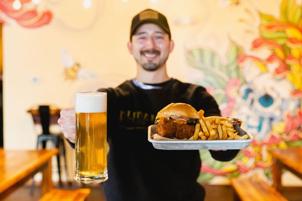 a server holds a stein of beer and a tray with a hamburger and fries