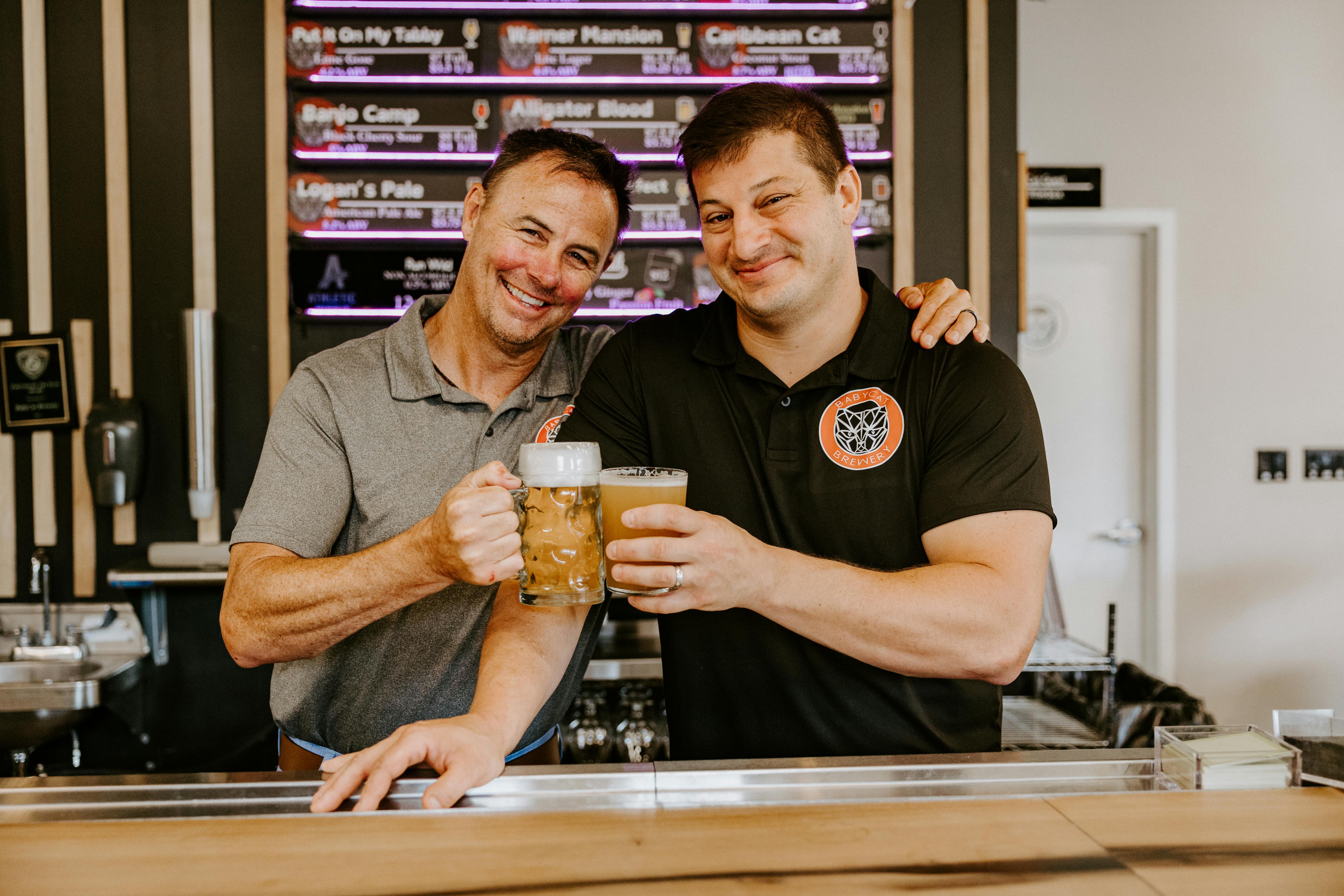 Baby Cat Owners of Babycat Brewery smiling holding beers behind the bar