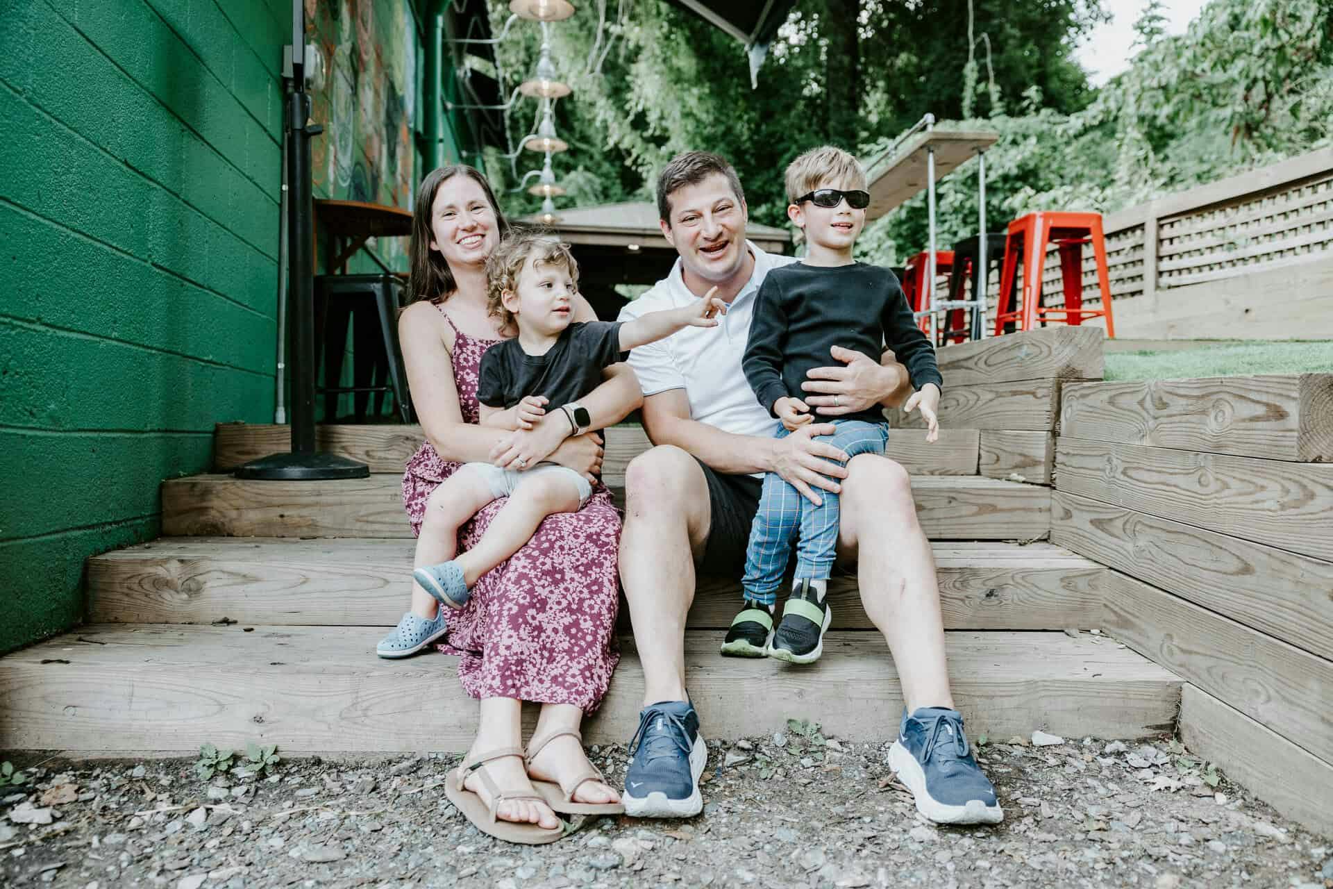 KSG25659 Babycat owner, Sam, sits on steps with his wife and two children