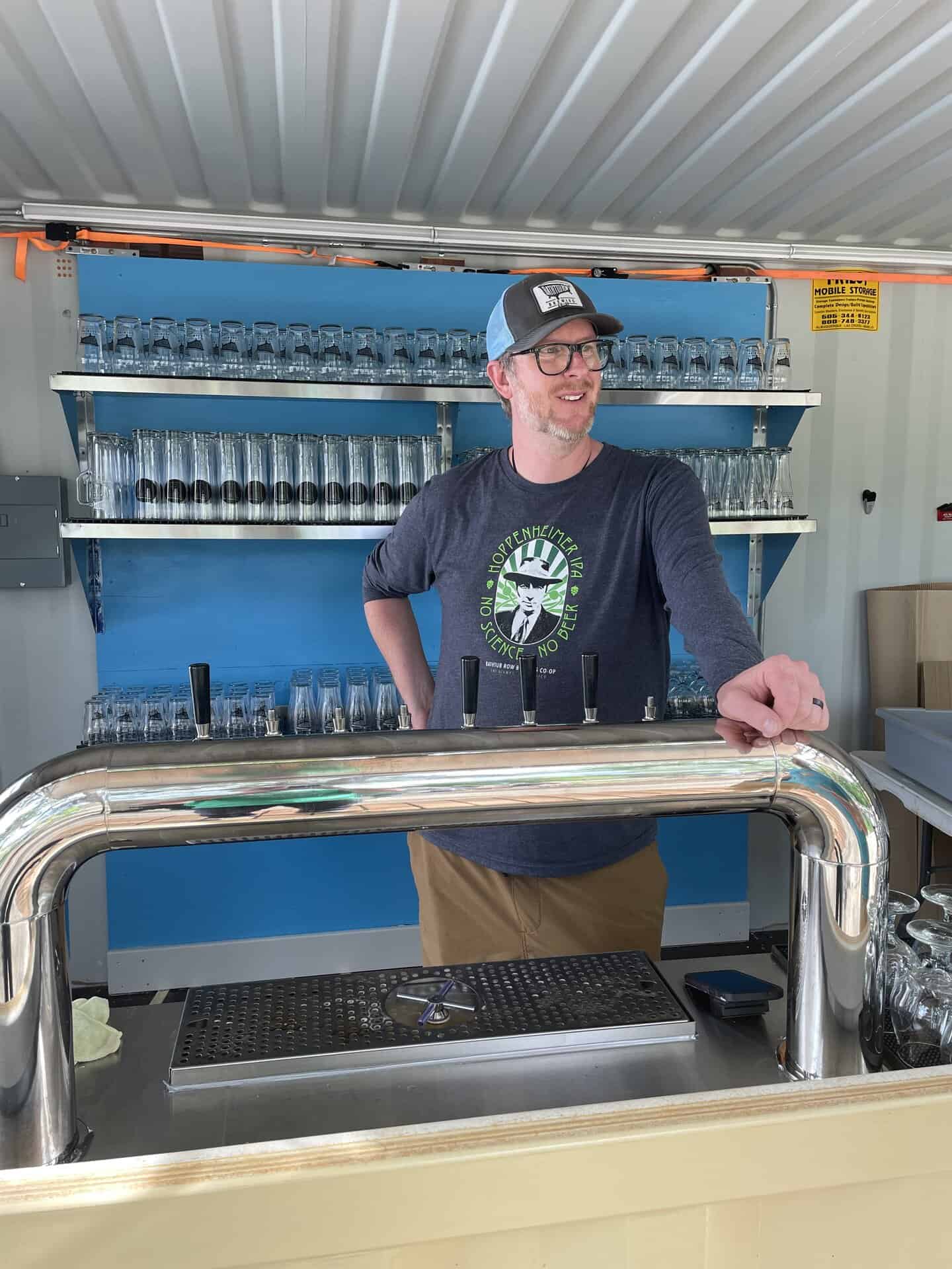 A man stands behind a tap bar with glassware behind