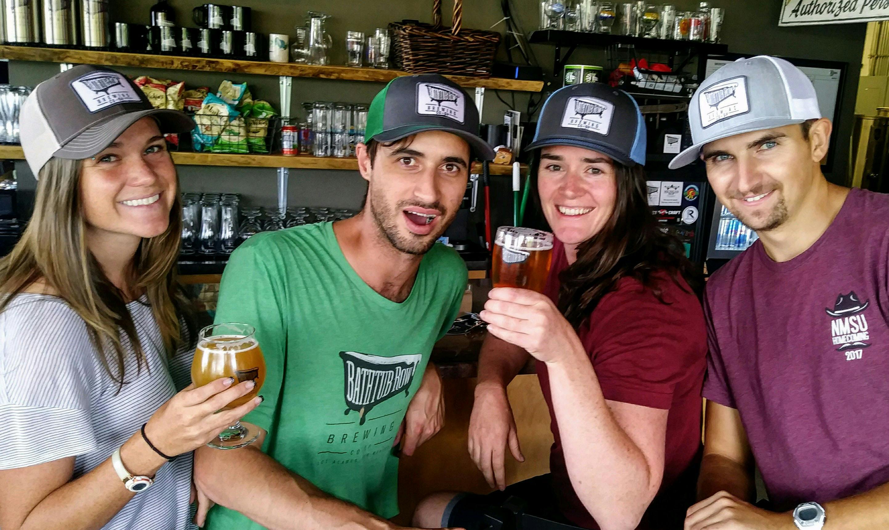 Four people wearing bathtub row brewing merch enjoy beers at the bar 