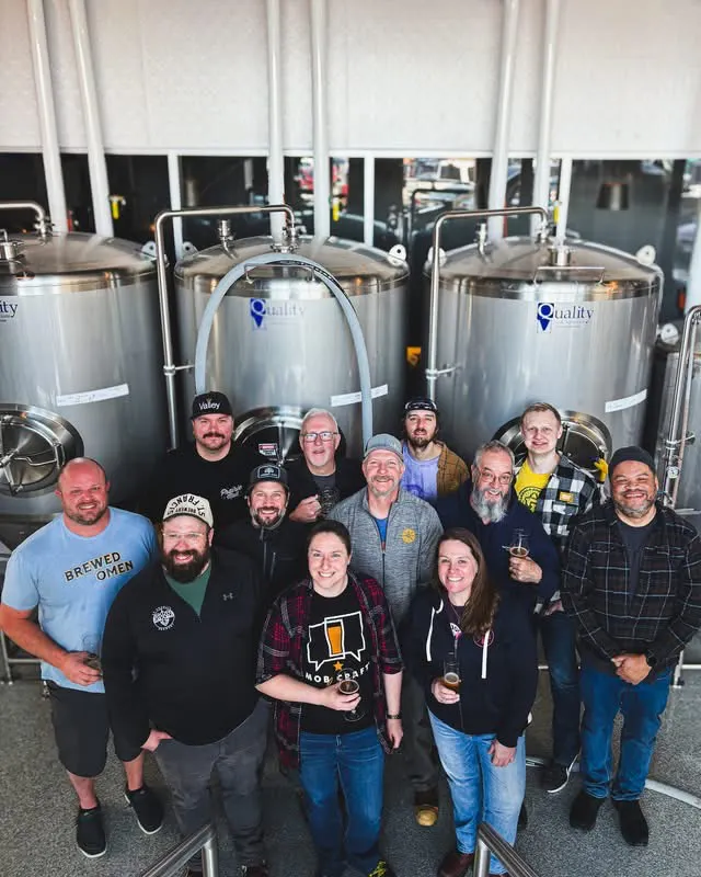 A group of people in front of 3 large stainless steel vessels