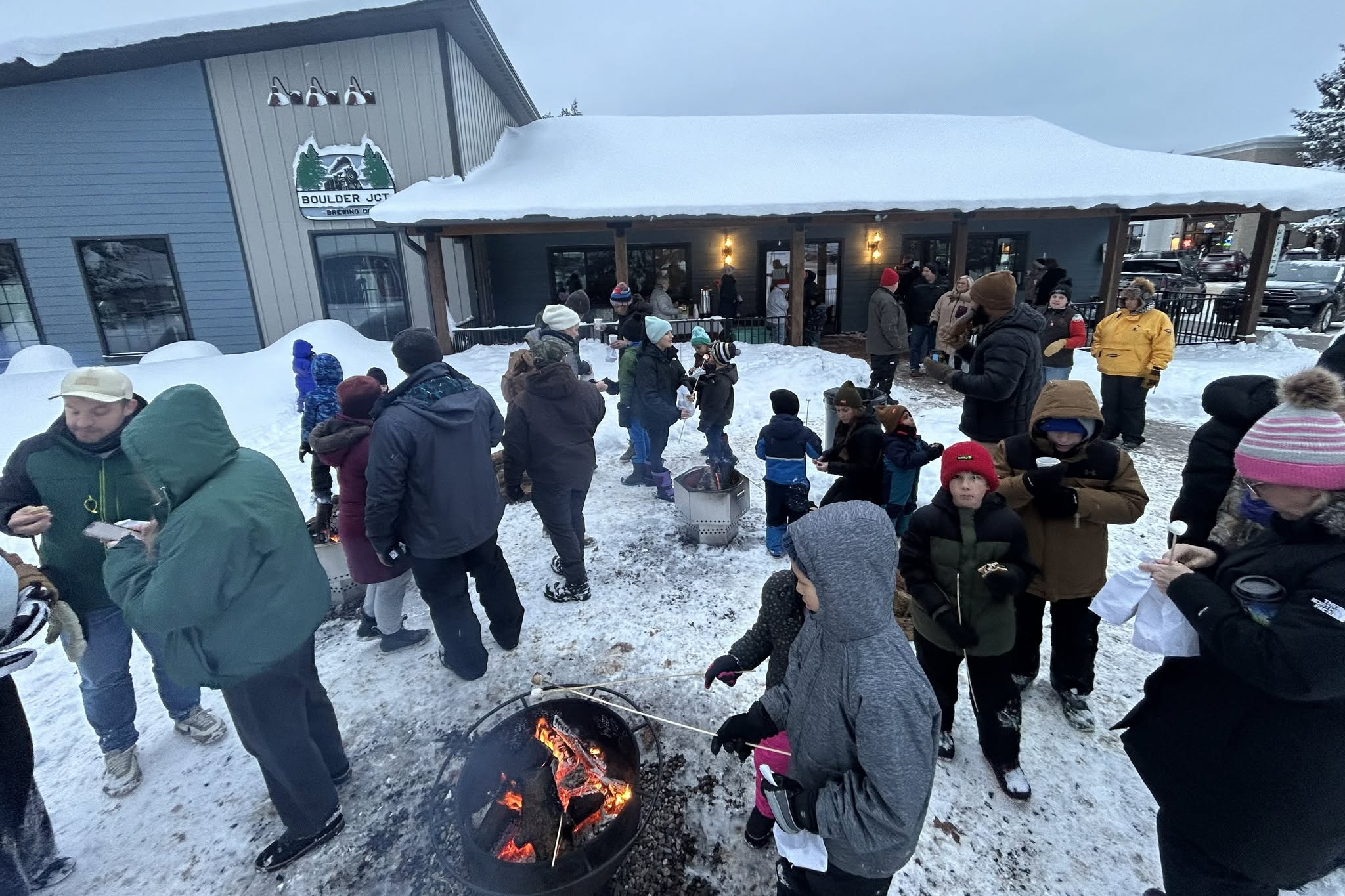 snowy beer garden with lots of people standing around fire pits roasting marshmallows