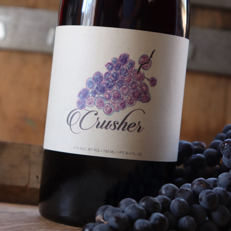Close up image of Crusher next to Merlot Grapes on a wine barrel