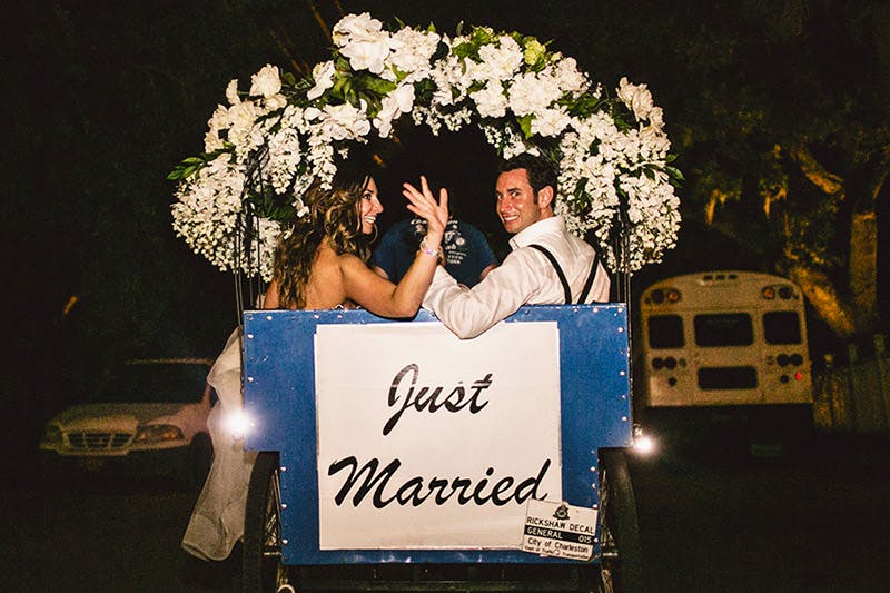Couple waves at guests as they depart in a pedicab that reads Just Married