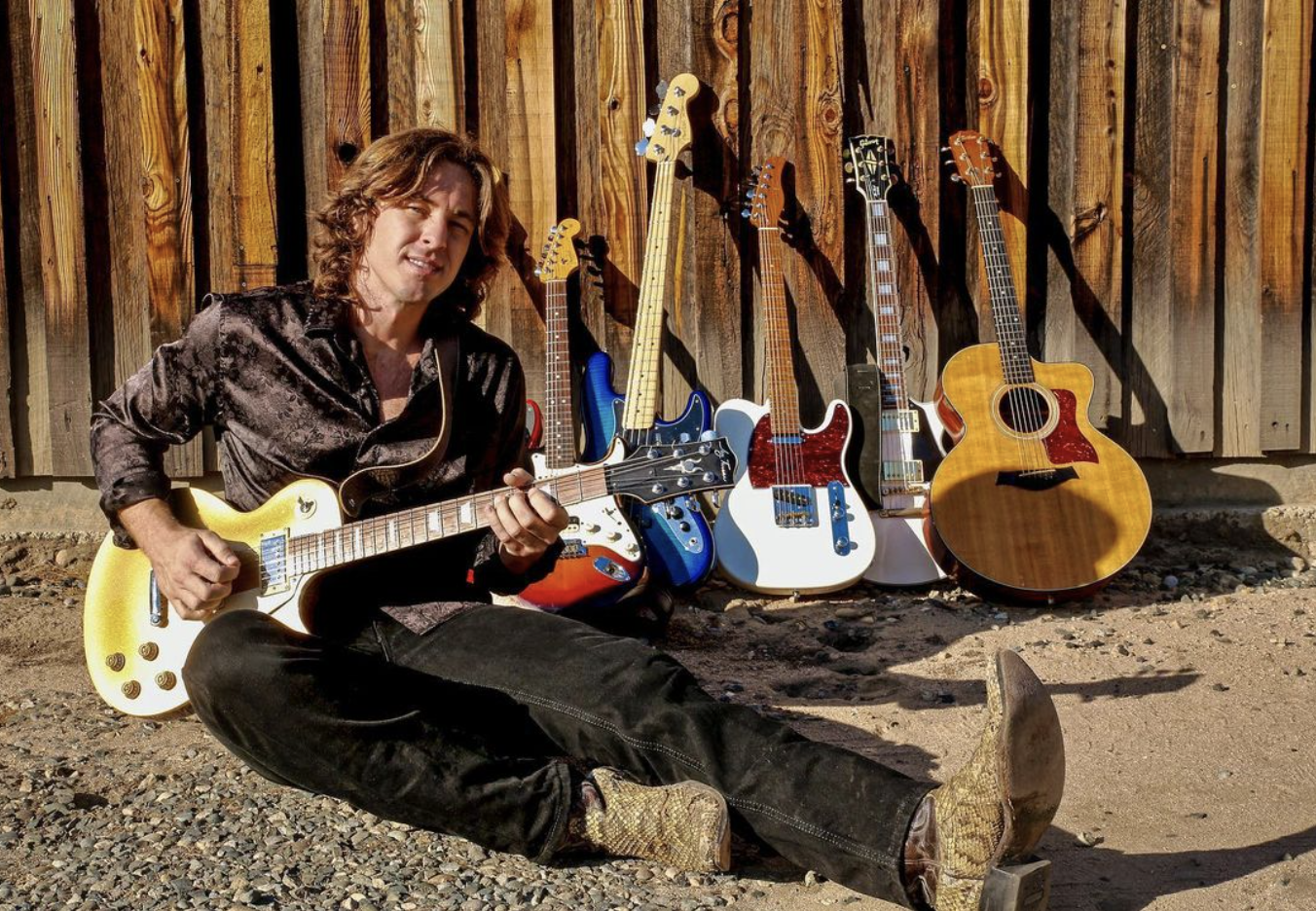 Erick Tyler playing the guitar with 5 guitars behind him 