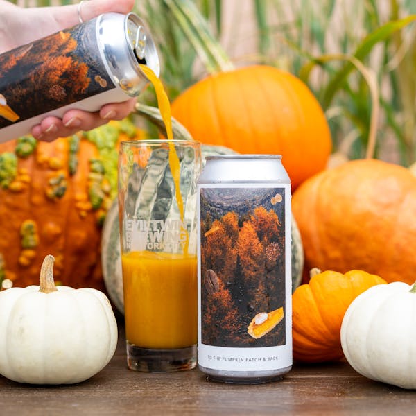 orange beer pouring in glass on table with pumpkins