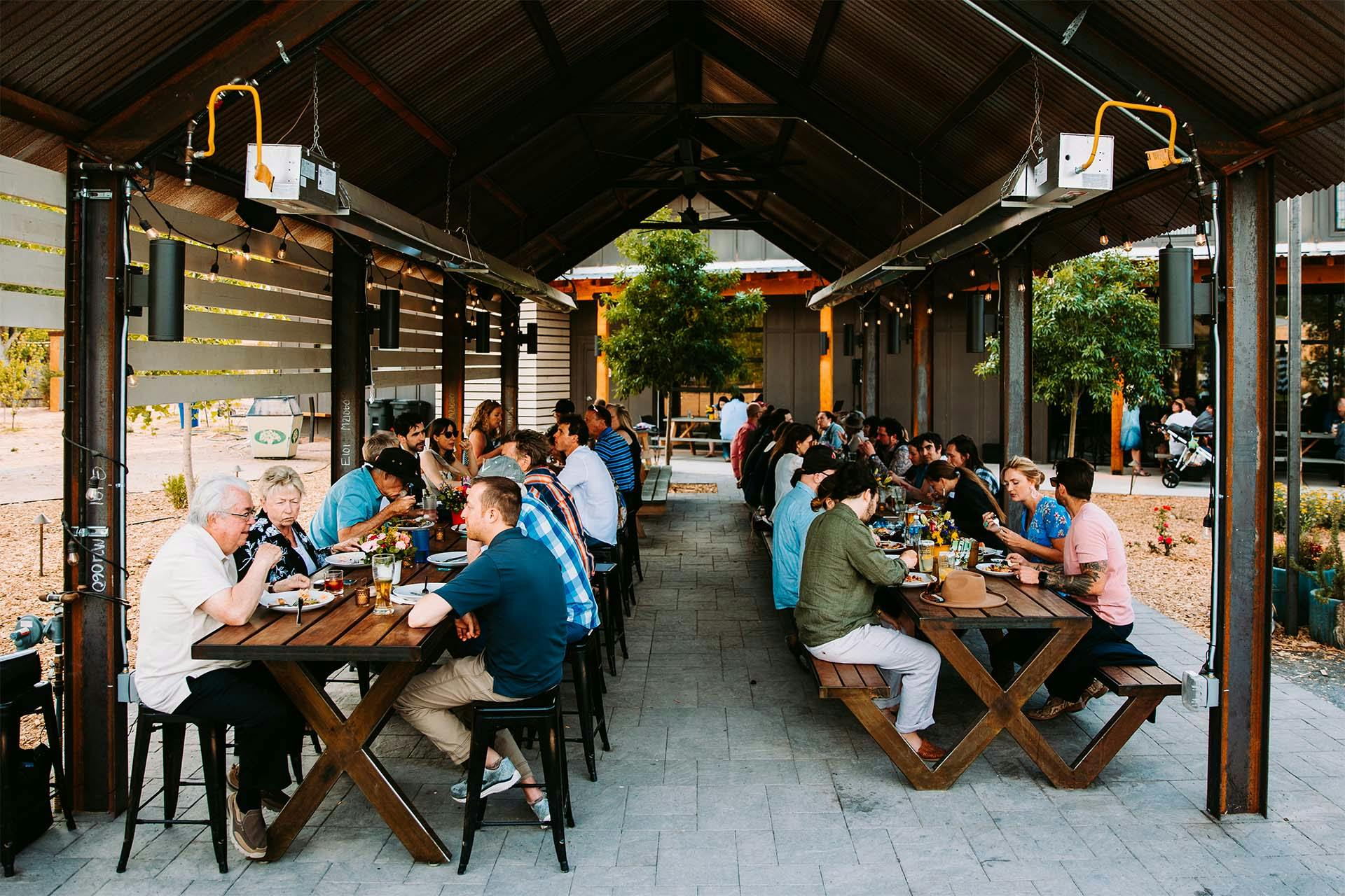 long tables outdoors with people seated enjoying food and beer