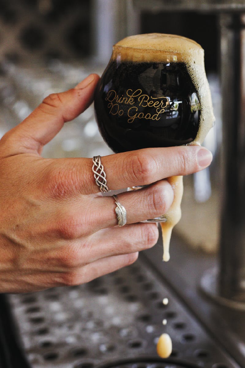 hands hold a small glass with dark beer in it