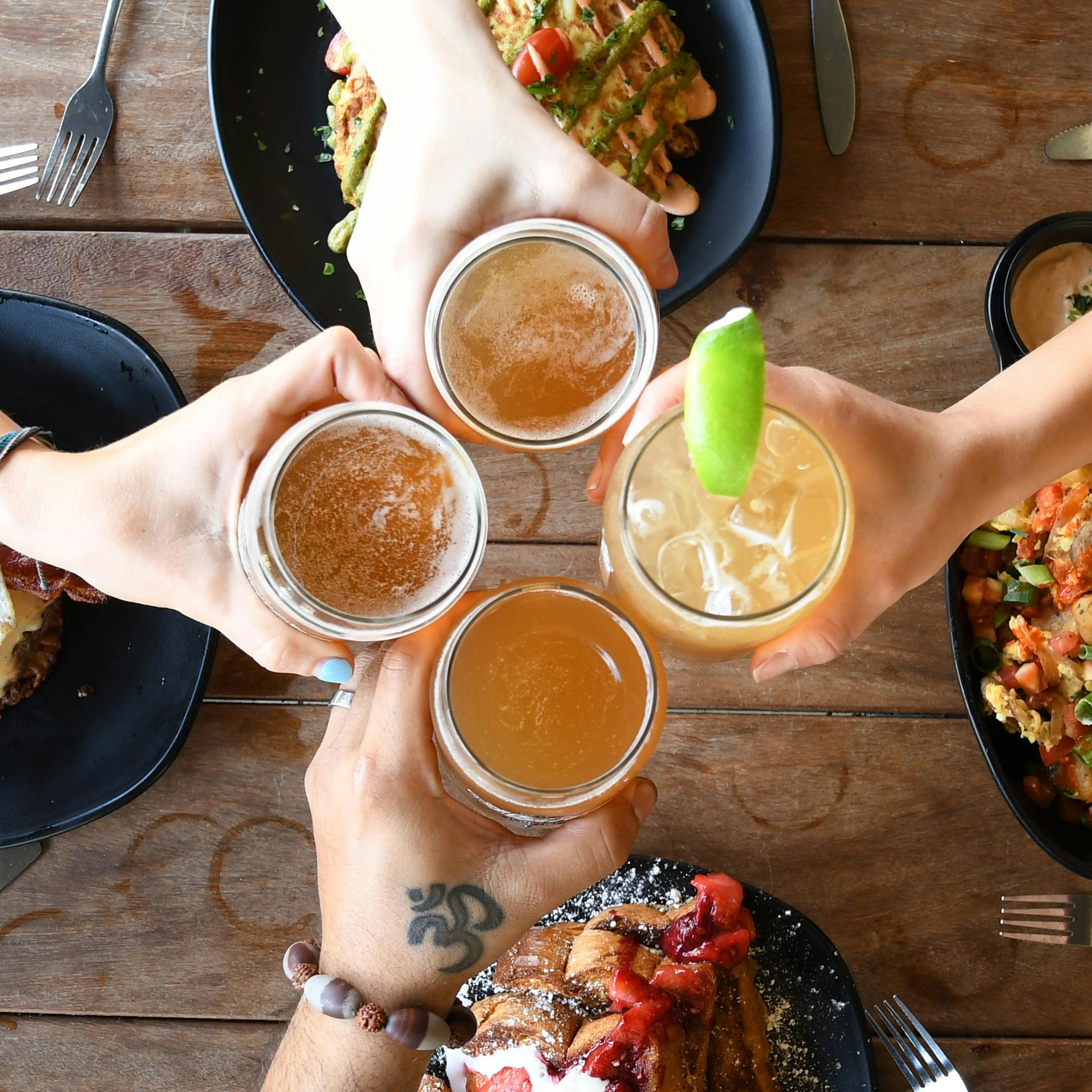 NYBRUNCH Hands holding beer glasses over food
