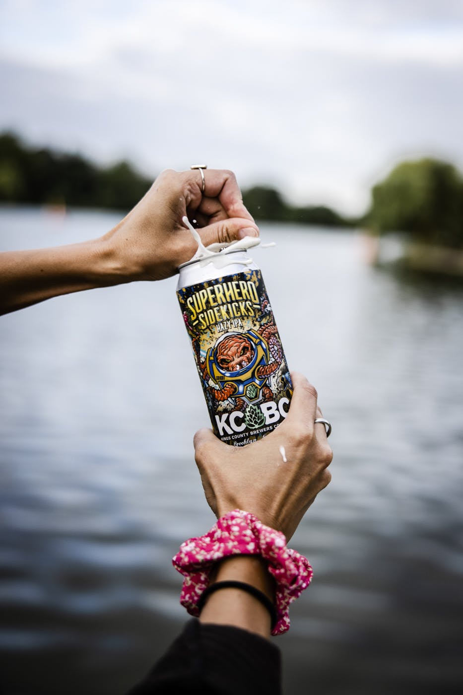 womens hand opening a KCBC beer near a lake