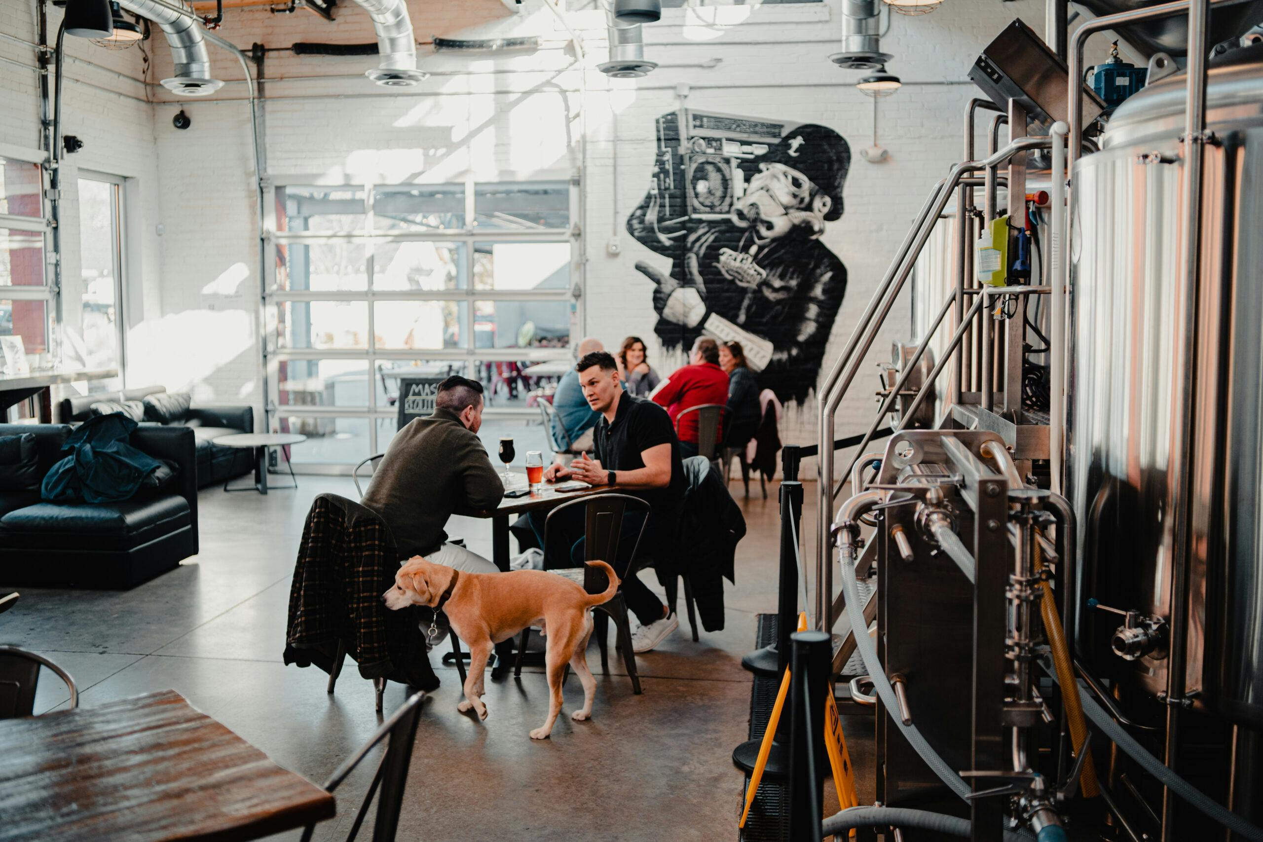 two guys enjoy a beer with their dog in the taproom