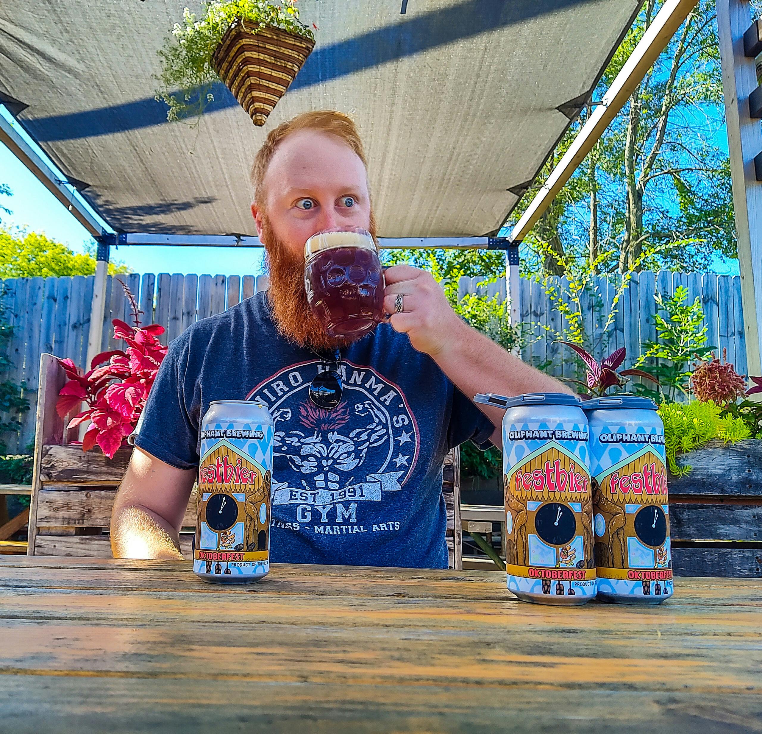man drinks beer outside of the taproom making a funny face