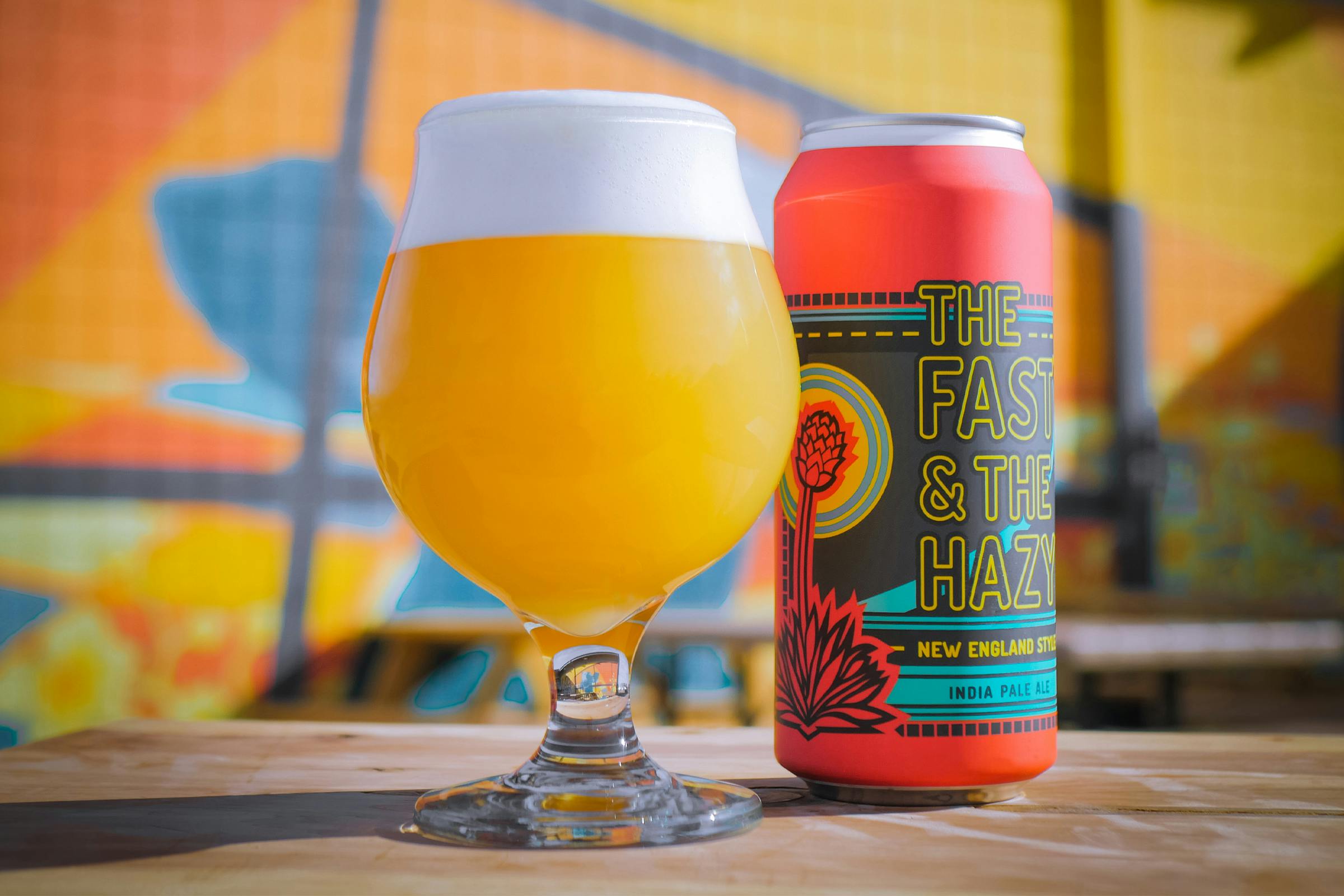 Our Story-1 A glass of beer and it's can on a table in front of a colorfully painted wall