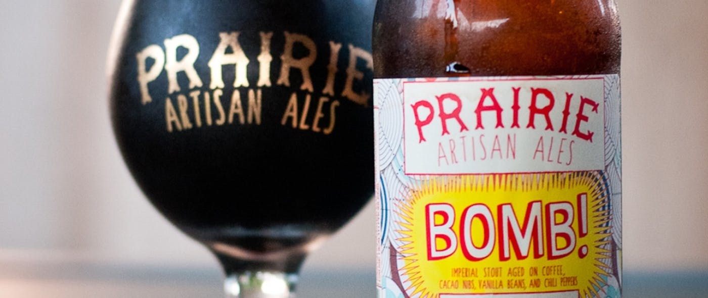 Close-up image of a dark beer in a Prairie Artisan Ales glass, and a beer bottle with Bomb label