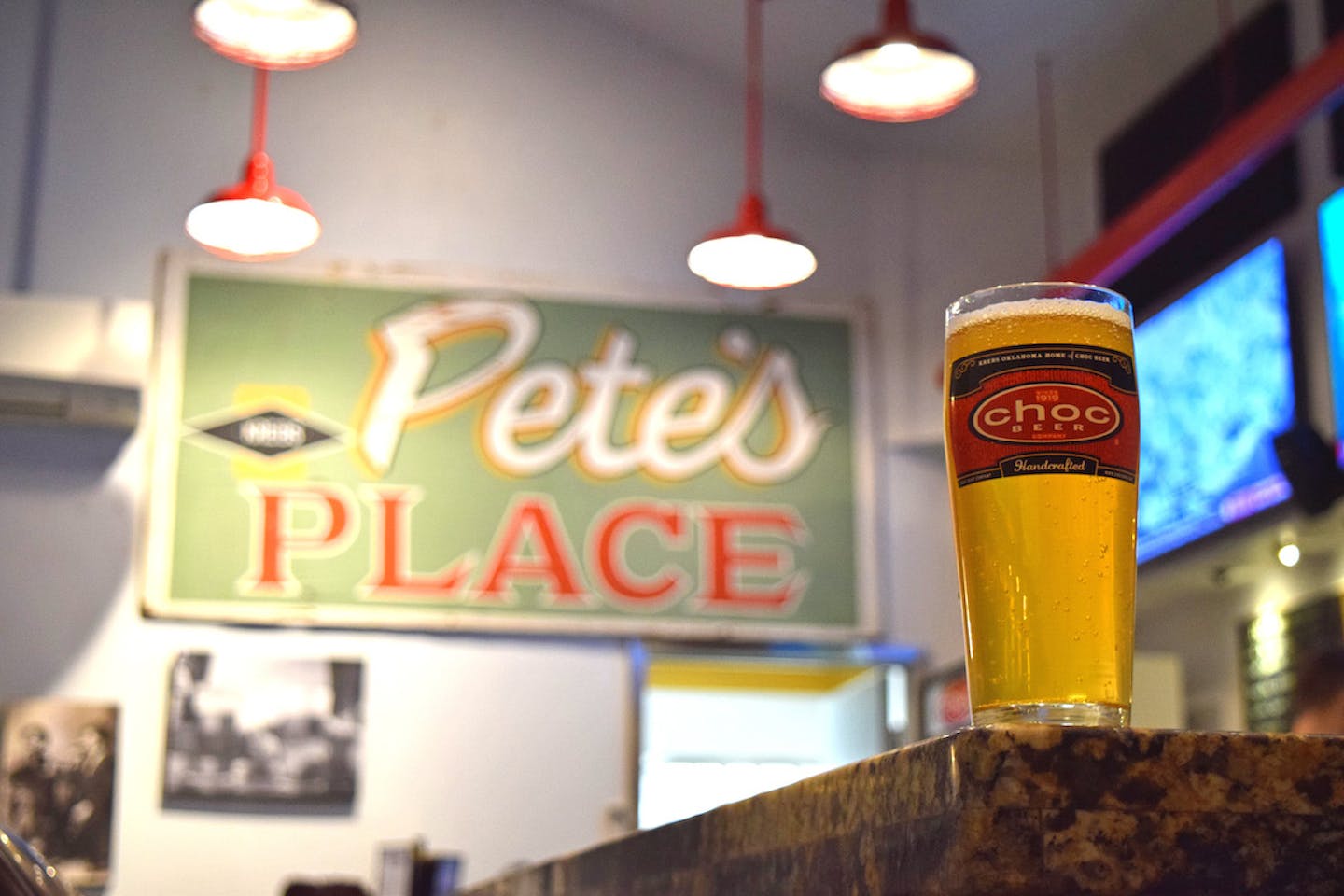 A glass of beer on a bar in front of a large sign teat reads, "Pete's Place"