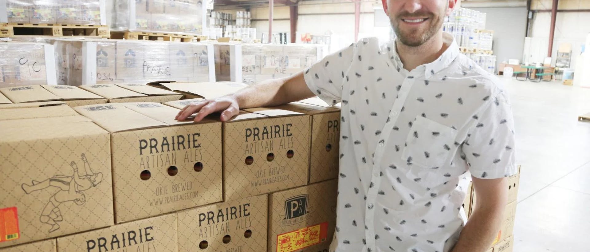 A man stands next to a stack of boxes of Prairie beer