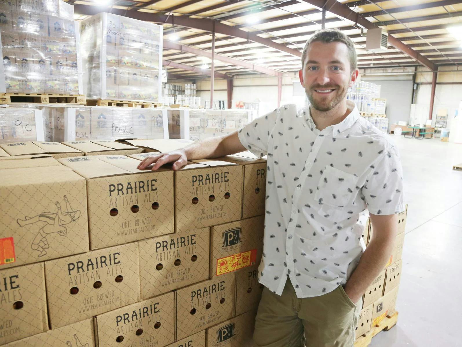 A man stands next to a stack of boxes of Prairie beer