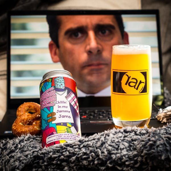 Glass of RaR Beer next to a 16 oz. can with Michael Scott from The Office on a screen behind