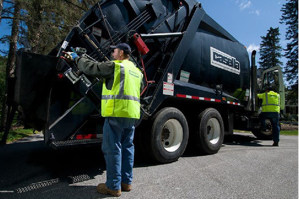 Photograph of Casella recycling truck with two operators wearing neon yellow vests.  One standing at the back of the truck another stepping into the cabin. 