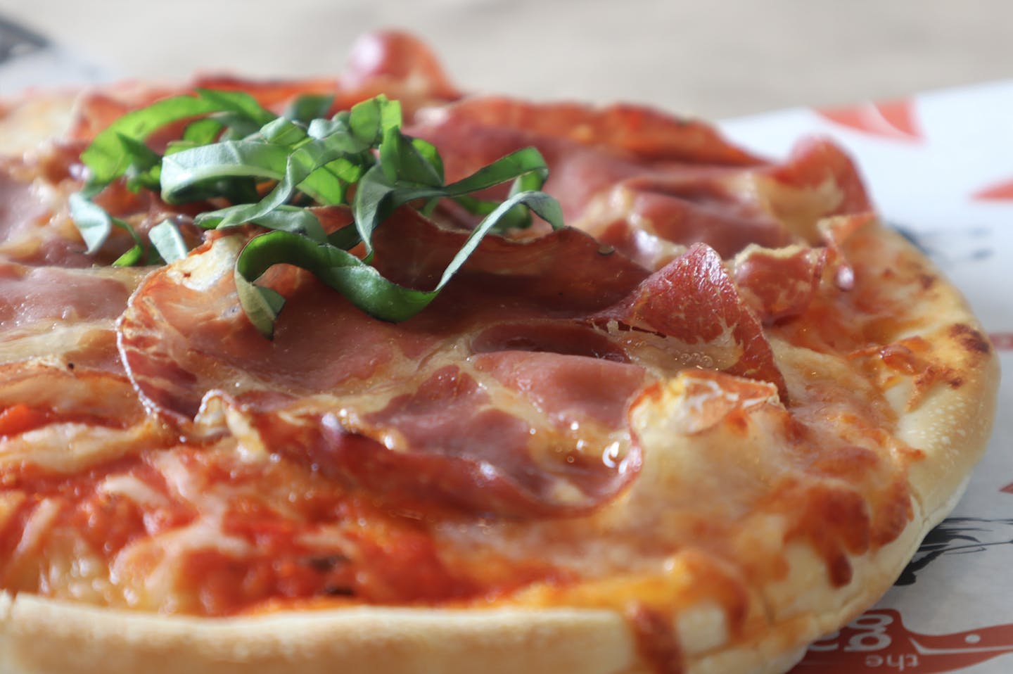 Close-up of personal meat pizza with large slices of prosciutto and fresh basil 
