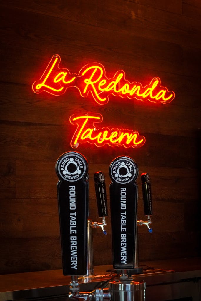 Neon red sign saying "La Redonda Tavern" with two black Round Table Brewery draft beer tap handles below it.