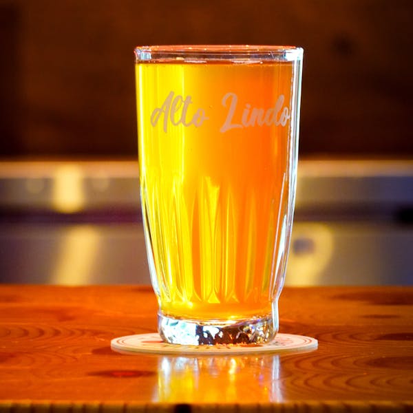 A golden bright rustic ale in a tall glass that says Alto Lindo on the brim.