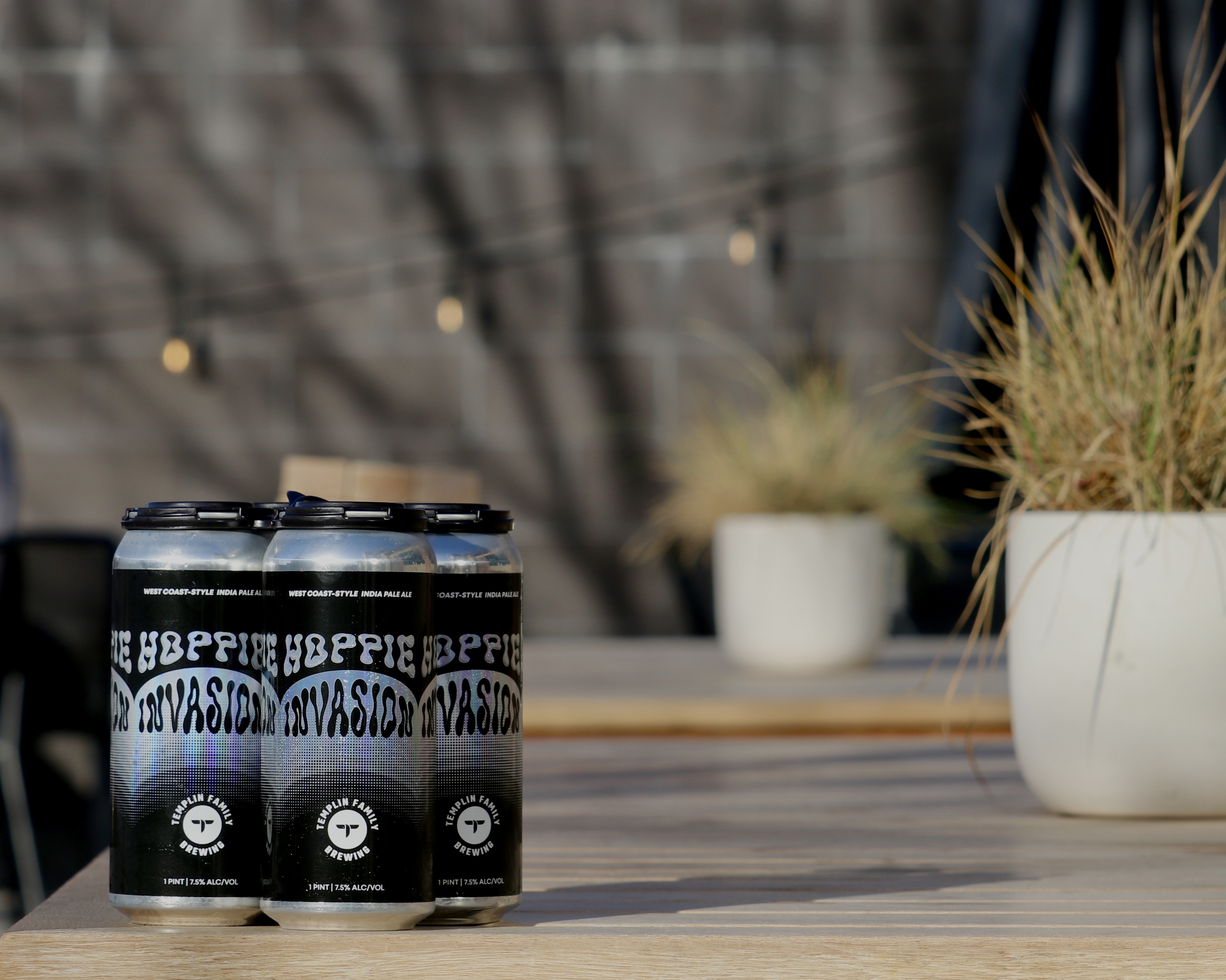 Picture of a 4 pack of beer called Hoppie Invasion with a back patio in the background