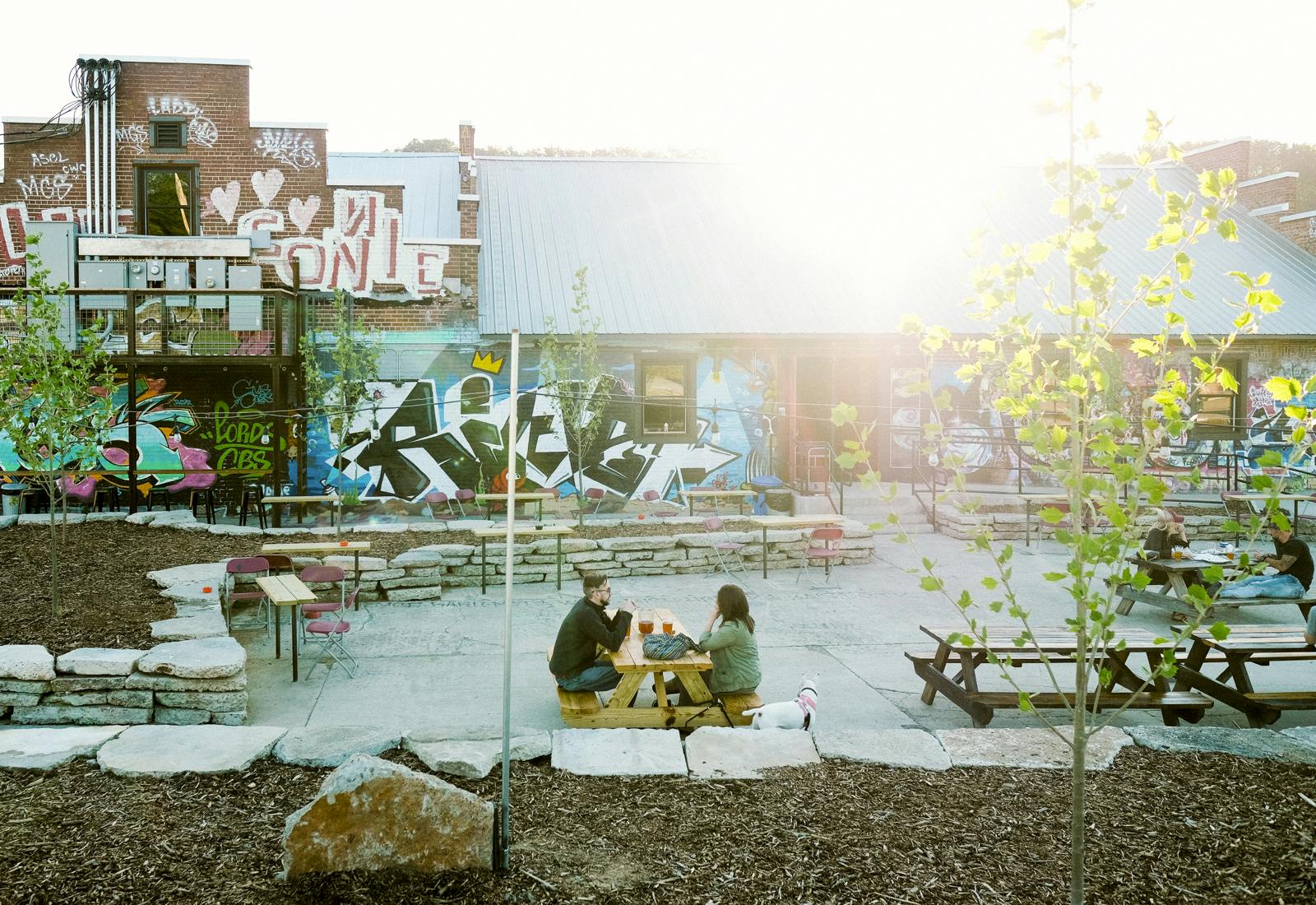 Two customers enjoy beers at a picnic table on a sunny day outside the Wedge Brewing taproom