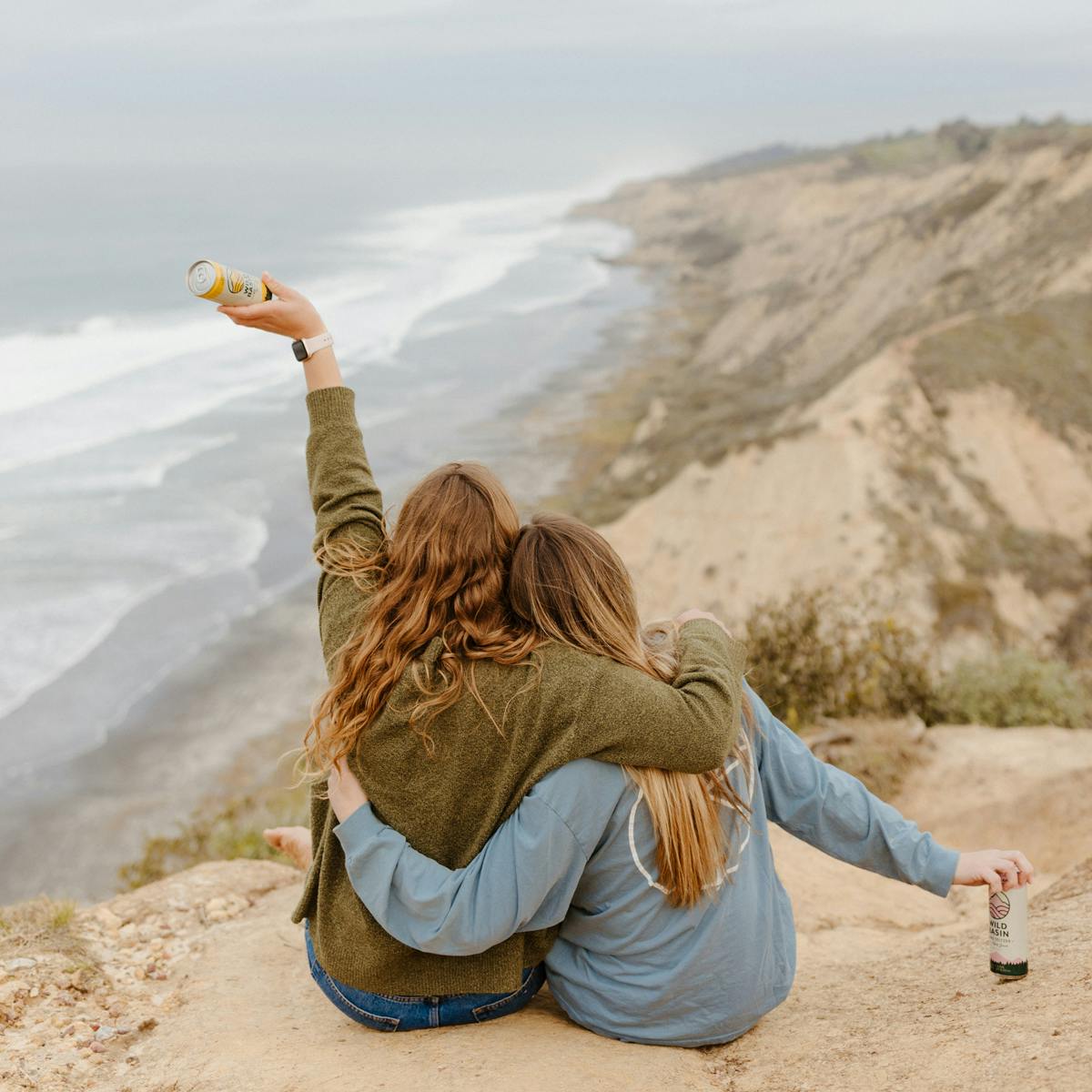 two girls sitting on a beach cliff with seltzers